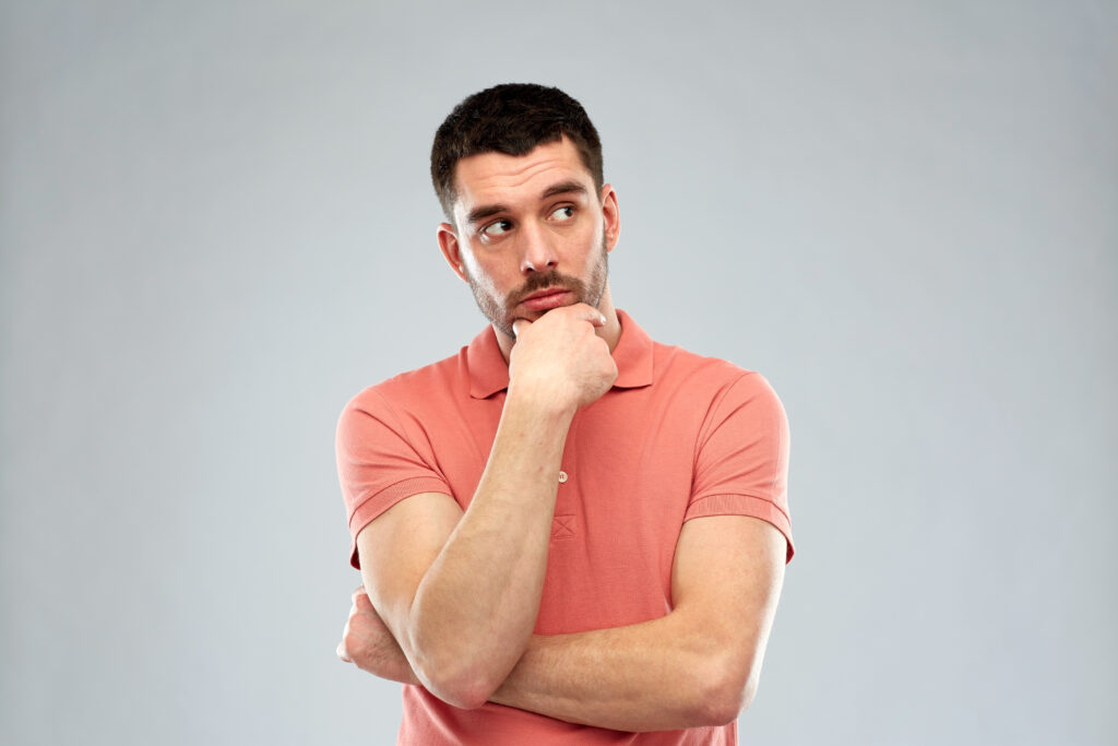 Imagem de um homem com camiseta coral, centralizada, com a mão no queixo pensativo.