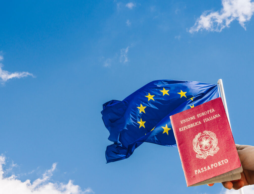 Bandeira da União Europeia (UE) contra um céu azul com uma mão segurando um passaporte italiano