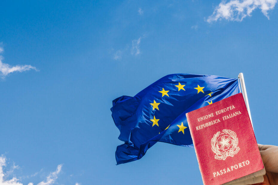 Bandeira da União Europeia (UE) contra um céu azul com uma mão segurando um passaporte italiano