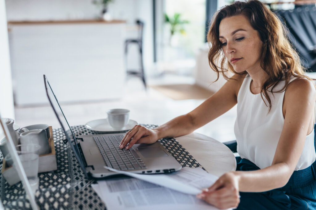 Mulher usando laptop enquanto senta à mesa. Jovem empresária sentada na cozinha e trabalhando no laptop.