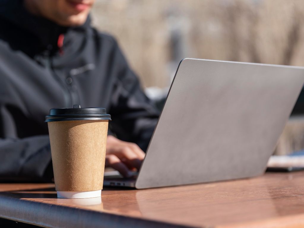 Imagem de uma pessoa com notebook na cafeteria para ilustrar conteúdo sobre visto para nômades digitais.